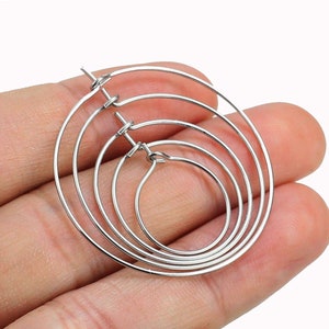 May include: Four silver hoop earrings of different sizes, stacked on top of each other.