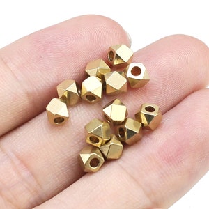 Puede incluir: Primer plano de una mano sosteniendo un grupo de cuentas de metal de color dorado. Las cuentas tienen forma de pequeñas pirámides multifacéticas.