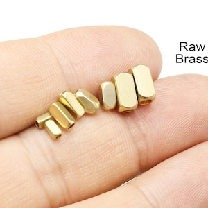 Puede incluir: Primer plano de varias cuentas de latón en bruto de varias formas. Las cuentas son de color dorado brillante y tienen un diseño geométrico. El texto "Raw Brass" es visible en la esquina superior derecha.