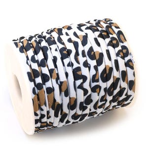 May include: A spool of leopard print ribbon. The ribbon features a white background with black and brown spots. The ribbon is tightly wound on a white spool, ready for crafting or decorative use. The ribbon is made of a soft, flexible material.