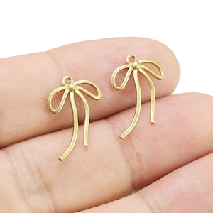 Pode incluir: Dois pingentes de metal dourado em forma de laço com um laço na parte superior para prender em joias ou artesanato.