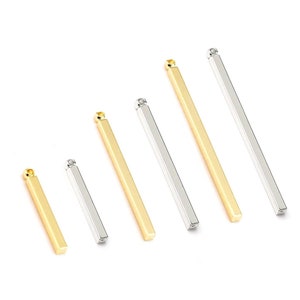 May include: A set of six gold and silver metal bar pendants, each with a loop at the top for attaching to a chain or cord. The bars are arranged in order of size, with the smallest bar on the left and the largest bar on the right.