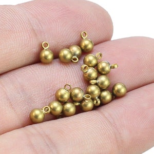 May include: A collection of gold-toned metal beads with a loop at the top. The beads are round and have a smooth finish.