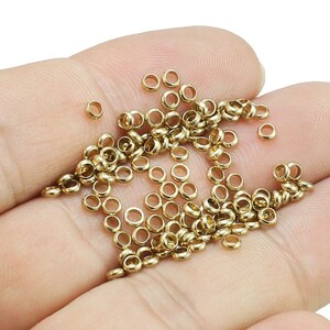 May include: A pile of gold-colored jump rings, also known as split rings, are shown in a hand. These rings are used for jewelry making and crafting.