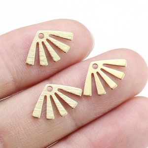 Puede incluir: Dos abalorios de metal dorado en forma de abanico con un agujero en la parte superior. Los abalorios miden aproximadamente 2,5 cm de ancho y 3,8 cm de alto.