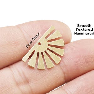 May include: A semi-circular raw brass jewelry component featuring a sunburst design with eight radiating rays and a single small hole at the top center. The text Raw Brass and Smooth Textured Hammered is printed near the metal piece.