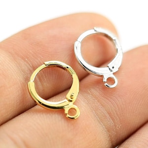 Könnte beinhalten: Zwei Ohrring-Verschlüsse, einer in Gold und einer in Silber, mit einem runden Ring und einem Hakenverschluss.