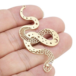 May include: Gold-toned metal snake charm with a cutout design featuring stars and a crescent moon. The snake is curled into a circle with its tail in its mouth.