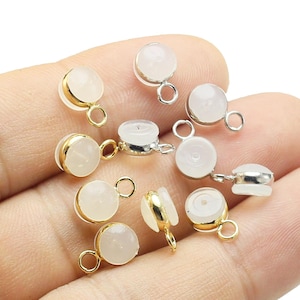 以下が含まれることがあります： 金と銀のジャンプリングが付いた白い丸いビーズの集まり。ビーズは手に置かれています。