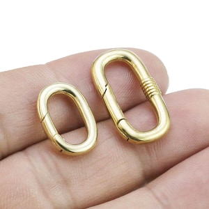 以下が含まれることがあります： 2つの金色の金属製の楕円形の留め具。留め具は開いており、チェーンやその他のジュエリーに取り付ける準備ができています。