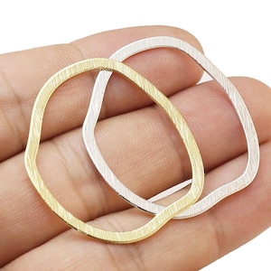 May include: Two open-shape metal jewelry findings. One is gold-toned, the other is silver-toned. Both have a textured surface and an irregular, wavy outline. The findings are held in a hand.