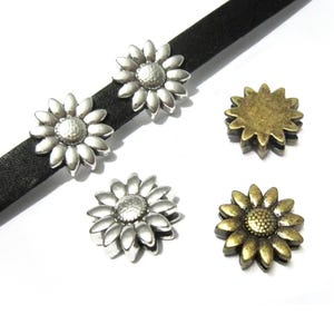 Peut inclure: Un cordon en cuir noir avec deux perles en forme de fleur argentées fixées dessus, accompagné de deux perles en forme de fleur supplémentaires, l'une argentée et l'autre bronze, chacune avec un centre texturé et de multiples pétales.