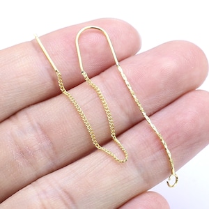 May include: A pair of gold earring findings with a chain and a loop at the end. The chain is a delicate, twisted design.