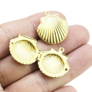 Könnte beinhalten: Drei goldfarbene Muschel-Anhänger aus Metall. Zwei der Anhänger sind mit Scharnieren versehen und lassen sich öffnen, um einen leeren Innenraum zu zeigen. Der dritte Anhänger ist eine einzelne Muschel.