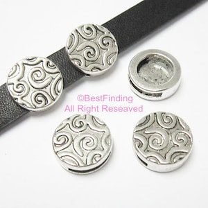 Puede incluir: Cuatro abalorios de metal plateados con un patrón de espiral. Los abalorios son redondos y tienen un agujero en el centro para sujetarlos a una pulsera o collar.