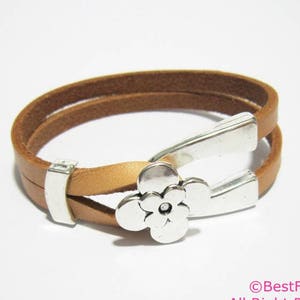 以下が含まれることがあります： 銀色の花の形をした留め具が付いた茶色の革のブレスレット。ブレスレットは二重になっており、シンプルなデザインです。