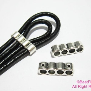 May include: Silver metal cord ends with four holes for threading leather cords. The cord ends are shown on a black leather cord.