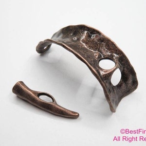 May include: A copper-toned metal bracelet with an open, organic design. The bracelet has a textured surface and a unique, asymmetrical shape.