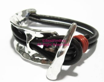Könnte beinhalten: Ein schwarzes Lederarmband mit einem silbernen Hakenverschluss. Das Armband hat ein geflochtenes Design und einen roten Akzent.