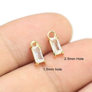 Peut inclure: Deux breloques en métal doré avec des pierres rectangulaires transparentes. Les breloques ont un trou de 1,5 mm et 2,5 mm.