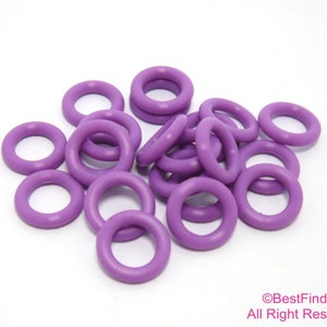 以下が含まれることがあります： 小さな丸い紫色のゴム製Oリングのコレクション。Oリングは均一な色で、柔軟な素材でできているようです。白い表面に散らばっています。