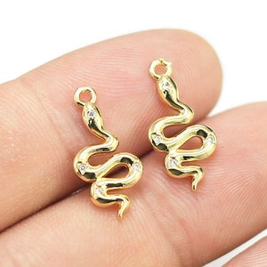 Puede incluir: Dos dijes de serpiente dorados con detalles de cristal transparente. Los dijes de serpiente tienen un bucle en la parte superior para sujetarlos a joyas.