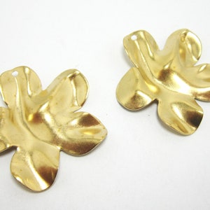 K&ouml;nnte beinhalten: Zwei goldfarbene Metall-Anh&auml;nger in Blumenform mit einem Loch oben zum Anbringen an Schmuck oder anderen Bastelarbeiten.