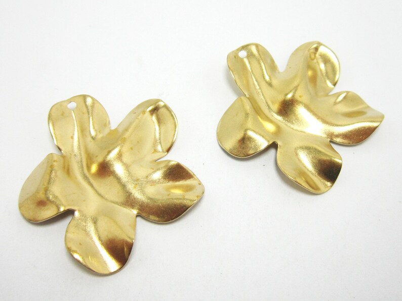 K&ouml;nnte beinhalten: Zwei goldfarbene Metall-Anh&auml;nger in Blumenform mit einem Loch oben zum Anbringen an Schmuck oder anderen Bastelarbeiten.
