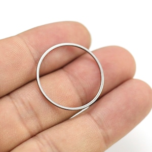 May include: A silver metal ring, possibly a washer or spacer, is held between two fingers.