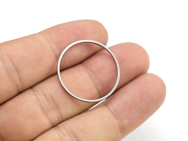 May include: A silver metal ring, possibly a washer or spacer, is held between two fingers.
