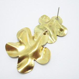 K&ouml;nnte beinhalten: Ein Paar goldfarbene, bl&uuml;tenf&ouml;rmige Ohrh&auml;nger. Die Ohrringe sind aus Metall und haben eine strukturierte Oberfl&auml;che.