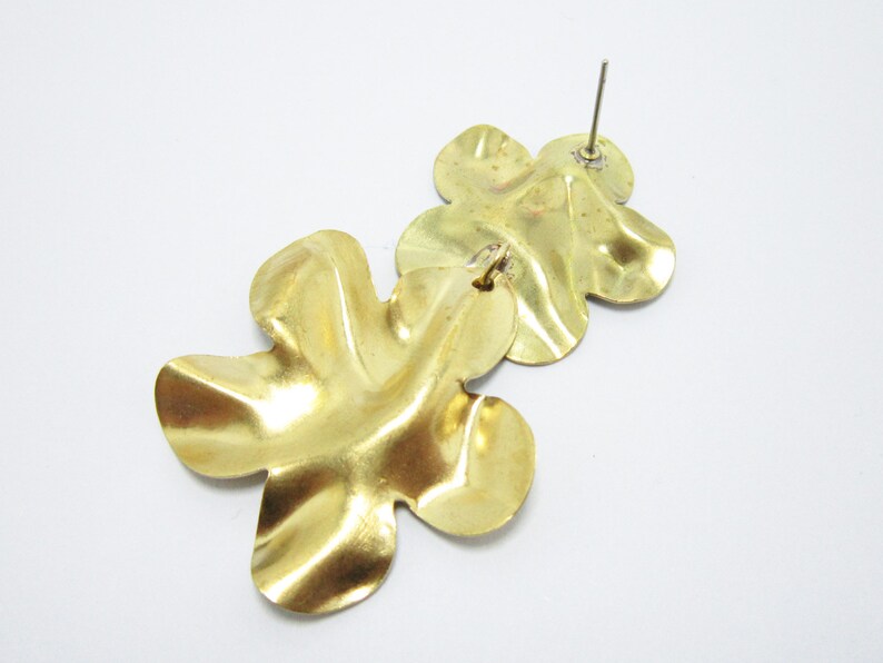 K&ouml;nnte beinhalten: Ein Paar goldfarbene, bl&uuml;tenf&ouml;rmige Ohrh&auml;nger. Die Ohrringe sind aus Metall und haben eine strukturierte Oberfl&auml;che.