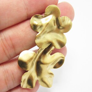K&ouml;nnte beinhalten: Zwei goldfarbene Metall-Blumenanh&auml;nger mit strukturierter Oberfl&auml;che. Die Anh&auml;nger sind an der Basis verbunden und haben eine leicht unregelm&auml;&szlig;ige Form.