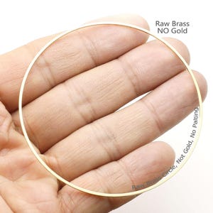 以下が含まれることがあります： 「Raw Brass Circle, Not Gold, No Plating」という文字が刻まれた、直径3.8cmの真鍮製の円形。円は手で持たれており、真鍮の色合いがわかります。
