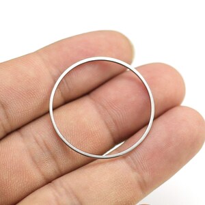 May include: A silver metal ring, shown held in a hand, is a simple, circular shape.