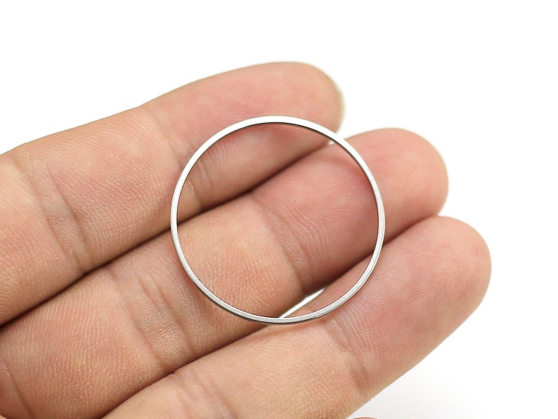 May include: A silver metal ring, shown held in a hand, is a simple, circular shape.