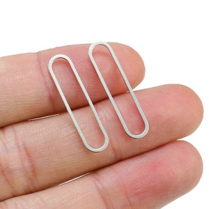 May include: Two silver oval-shaped earrings. The earrings are simple and minimalist in design.