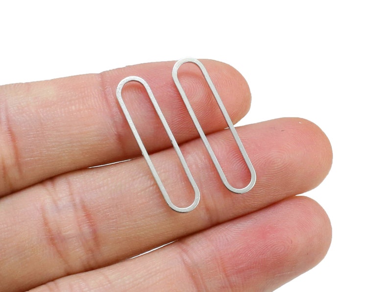 May include: Two silver oval-shaped earrings. The earrings are simple and minimalist in design.