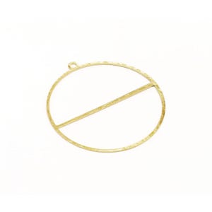 May include: A gold-toned metal pendant featuring a large circular frame with a single horizontal bar running across the center. The surface of the metal has a textured, hammered finish and includes a small circular loop at the top for attachment.