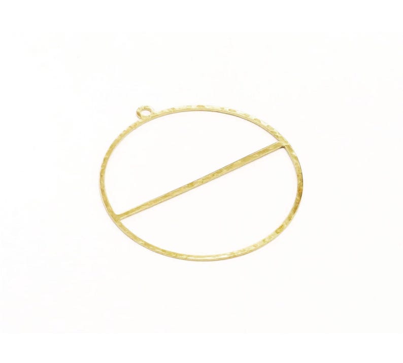 May include: A gold-toned metal pendant featuring a large circular frame with a single horizontal bar running across the center. The surface of the metal has a textured, hammered finish and includes a small circular loop at the top for attachment.