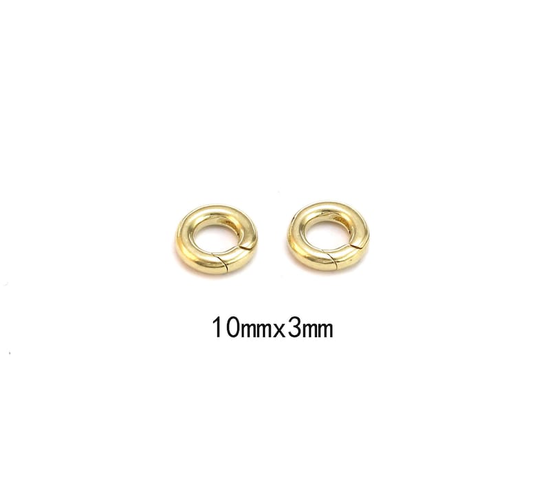 Pode incluir: Duas fivelas circulares douradas com abertura articulada. As fivelas t&ecirc;m 10 mm de di&acirc;metro e 3 mm de espessura. As fivelas est&atilde;o em um fundo branco. Provavelmente s&atilde;o usadas para fazer joias ou outros artesanatos.