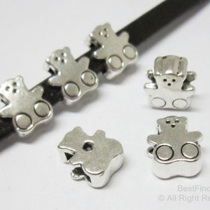 May include: Silver-toned metal teddy bear charms with a hole for threading. The charms are about 1 inch in size and have a smooth, shiny finish.
