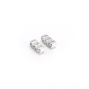 May include: Two silver metal spacers with three round holes each. The spacers are designed to be used in jewelry making.