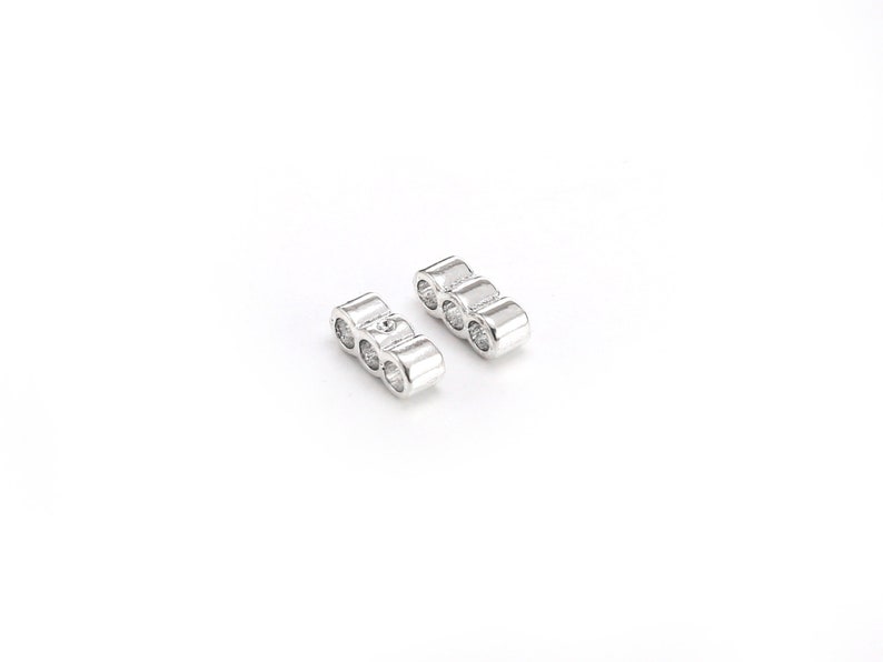 May include: Two silver metal spacers with three round holes each. The spacers are designed to be used in jewelry making.