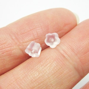 Puede incluir: Dos pequeños topes de pendientes translúcidos en forma de flor. Uno tiene forma de cubo y el otro de flor. Los topes de los pendientes están hechos de un material transparente, posiblemente plástico. El fondo es de color claro.