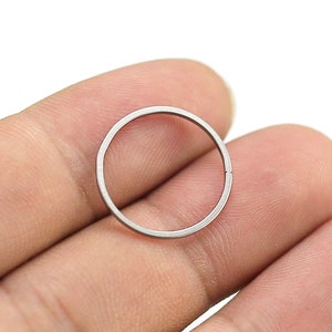 May include: A silver metal ring, approximately 1 inch in diameter, is held between two fingers.