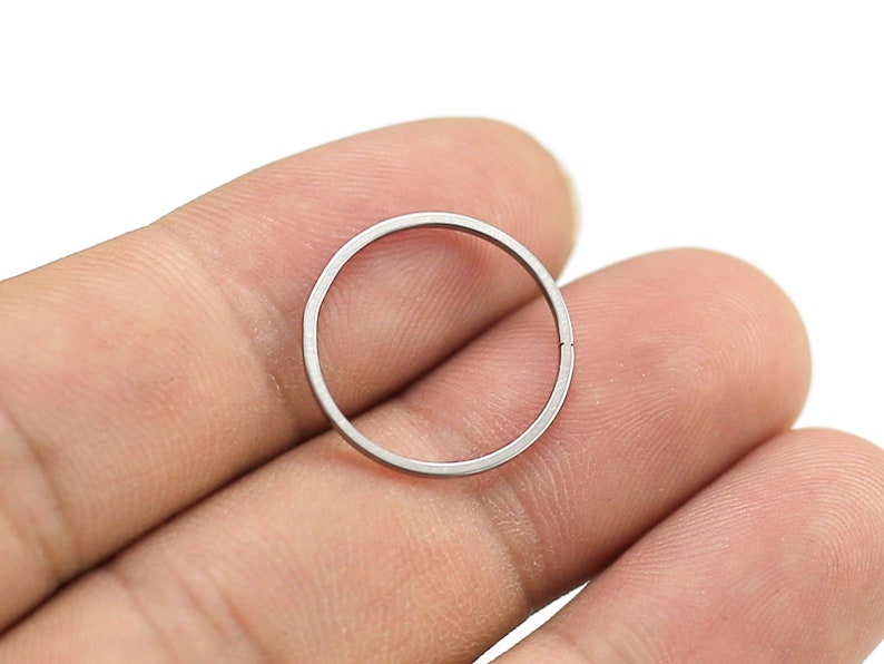 May include: A silver metal ring, approximately 1 inch in diameter, is held between two fingers.