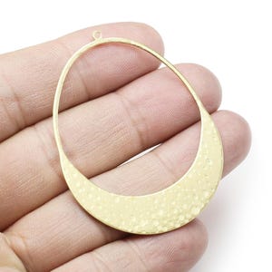 Puede incluir: Aro ovalado de metal dorado con textura martillada. El aro tiene un pequeño bucle en la parte superior para sujetarlo a joyas.