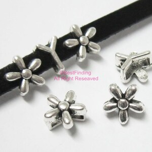 May include: Silver-colored daisy-shaped beads with a distressed finish. The beads are scattered on a white surface and a black velvet ribbon. The image includes the text "BestFinding All Right Reseaved".
