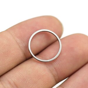 May include: A silver metal ring, approximately 1 inch in diameter, is held between two fingers.
